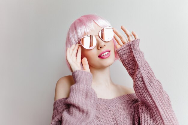 Foto gratuita ragazza graziosa pensierosa in periwig rosa che osserva in su sulla parete chiara. foto dell'interno di una donna elegante dai capelli corti in abbigliamento lavorato a maglia viola e peruke.