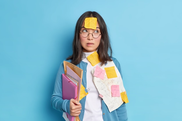 생각에 잠겨있는 의아해 여학생은 학교에서 시험을 준비하고 입술을 물고 집중하여 시력 교정을 위해 둥근 안경을 쓰는 수학 시험 전에 정보를 배우려고 노력합니다.