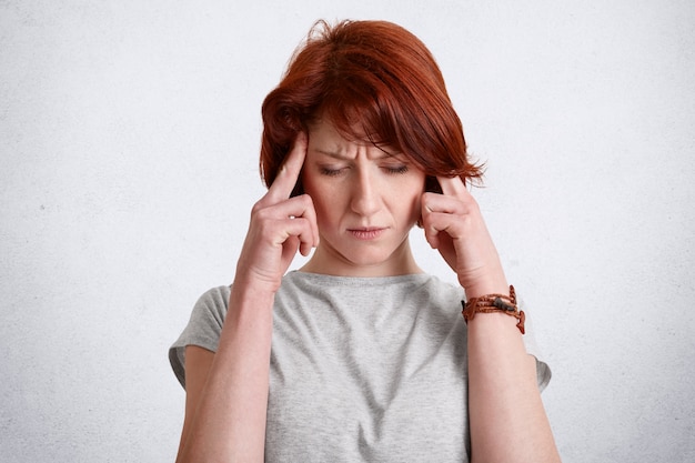 Pensive red haired concentrated female keeps fingers on temples