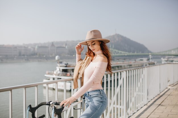 Pensive red-haired woman in hat posing on sky wall in weekend