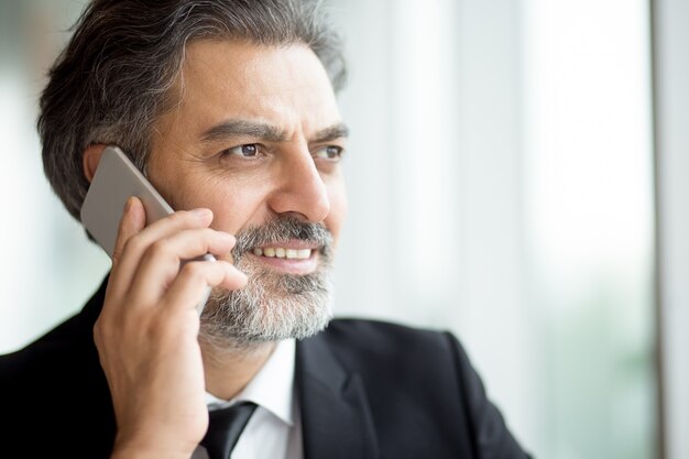 Pensive senior businessman with beard using phone