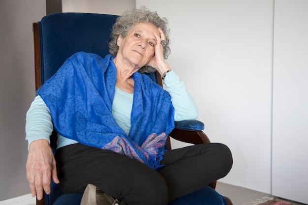 Pensive senior lady sitting in rocking chair and looking away