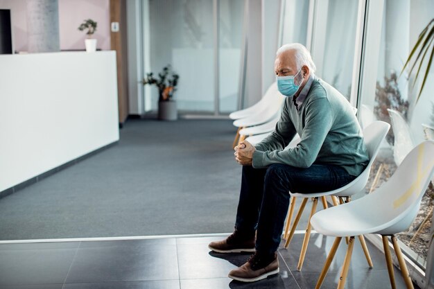 Pensive senior man with protective face mask sitting in waiting room at the hospital