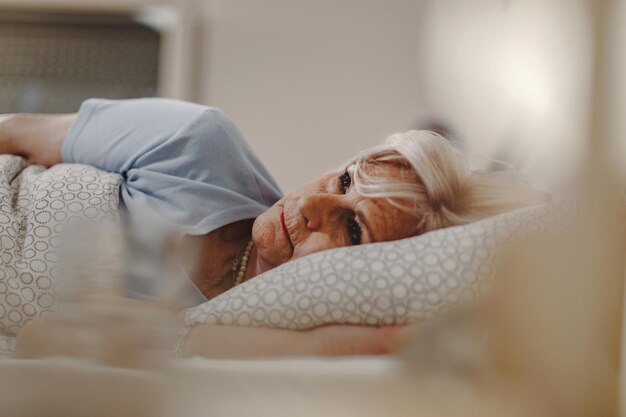 ベッドに横になって何かを考えている物思いにふける年配の女性