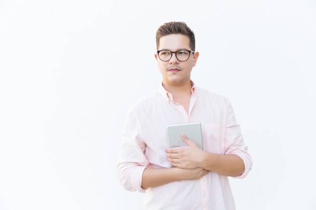 Pensive serious guy in eyeglasses embracing tablet