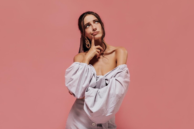 Free Photo pensive slim lady with tanned skin and brunette hair in gold accessories in wide sleeve lilac shirt looking up and posing