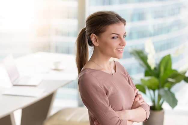 Foto gratuita giovane donna sorridente pensierosa che esamina finestra, armi attraversate, all'interno