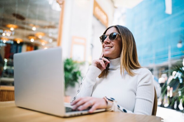 Pensive smiling young woman using laptop at table in street cafe