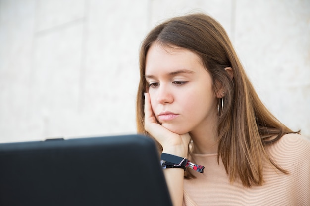 Задумчивый подросток девушка просматривает на ноутбуке на открытом воздухе