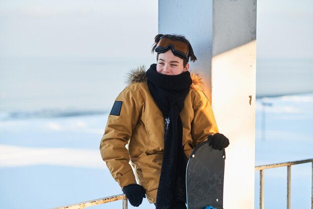 Pensive teen with snowboard in hands is posing for photographer at winter day.