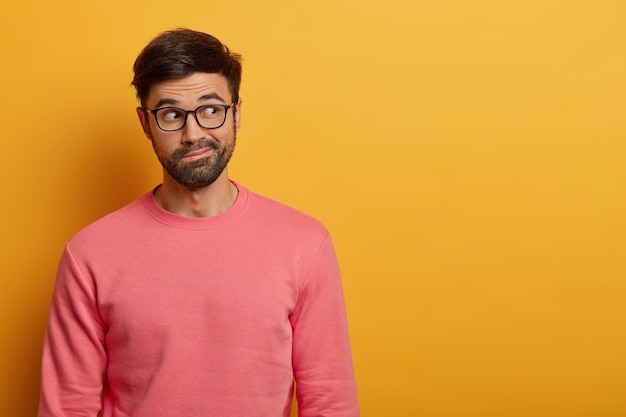 Pensive unshaven guy looks thoughtfully aside, purses lips