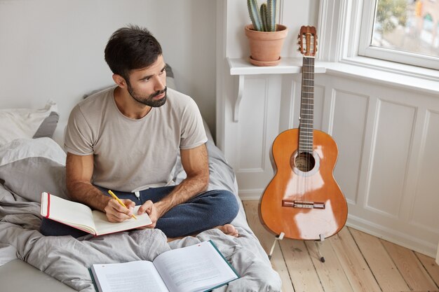 Pensive unshaven man sits in lotus pose on bed