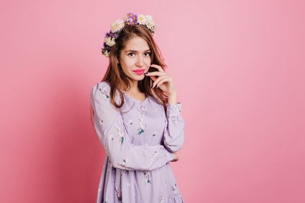 Pensive woman in flower wreath posing on pink wall