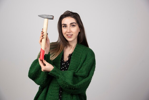 Pensive woman holding hammer in hands on a gray background.