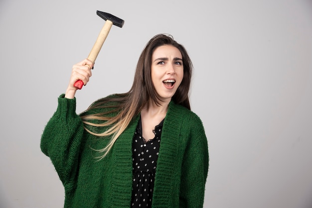 Free photo pensive woman holding hammer in hands on a gray background.