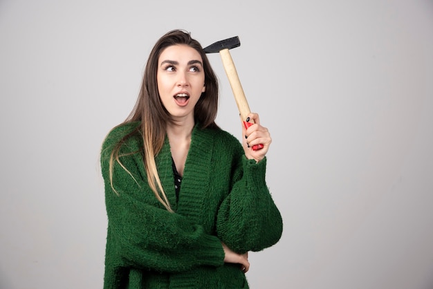 Pensive woman holding hammer in hands on a gray background.