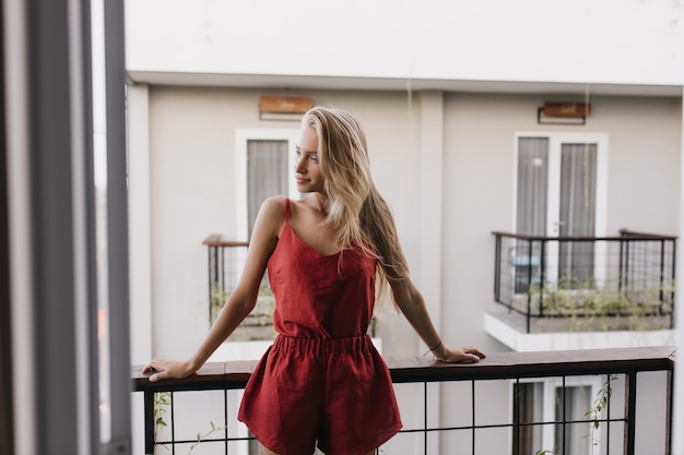 Pensive woman in pajama enjoying summer morning. Appealing long-haired woman standing at balcony.