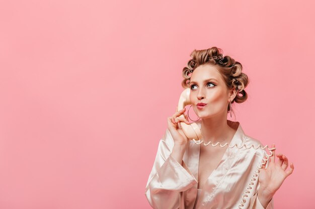 Pensive woman in silk robe talking on phone on isolated wall