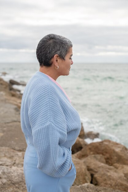 Pensive woman walking near sea. Female model with short hair having walk on cloudy day. Looking at water. Nature, spare time concept