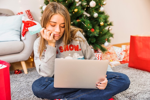 Pensive woman with credit card and laptop 