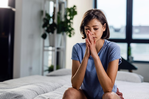 Pensive woman with hands clasped sitting on the bed and thinking of something
