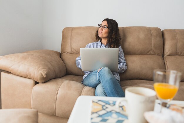 Задумчивый женщина с ноутбуком, сидя на диване