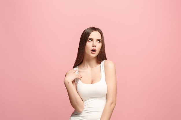 Pensive woman with thoughtful expression making choice against pink wall