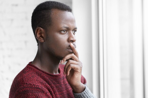 Pensive worried African American art director dressed casually keeping finger on lips