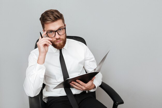 Pensive young businessman in eyeglasses holding a folder