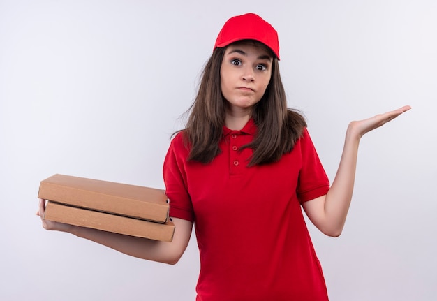 Pensieroso giovane donna di consegna che indossa la maglietta rossa in berretto rosso che tiene una scatola di pizza sul muro bianco isolato