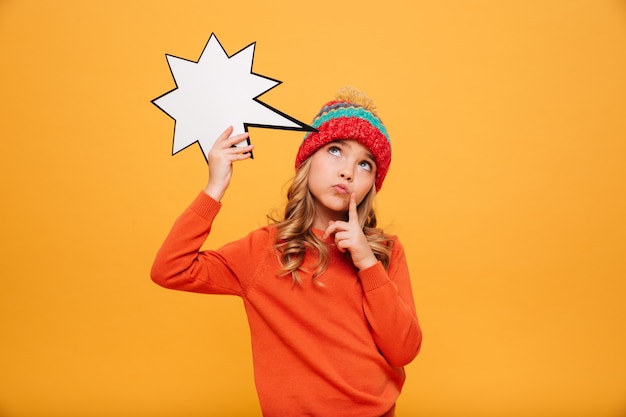 Бесплатное фото Задумчивая молодая девушка в свитере и шляпе держит пустую речь звездой и смотрит на апельсин