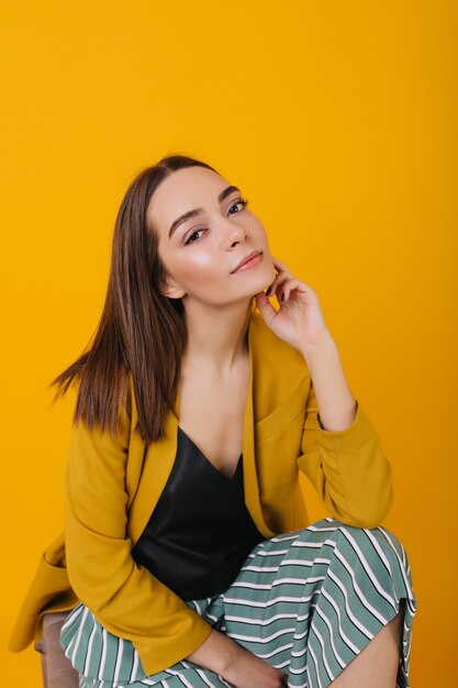 Pensive young lady in bright jacket sitting. Winsome female model with trendy haircut posing.