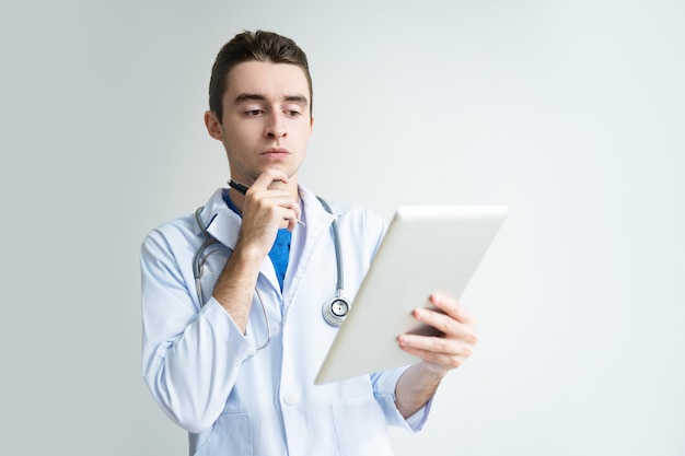 Pensive young male doctor using tablet computer