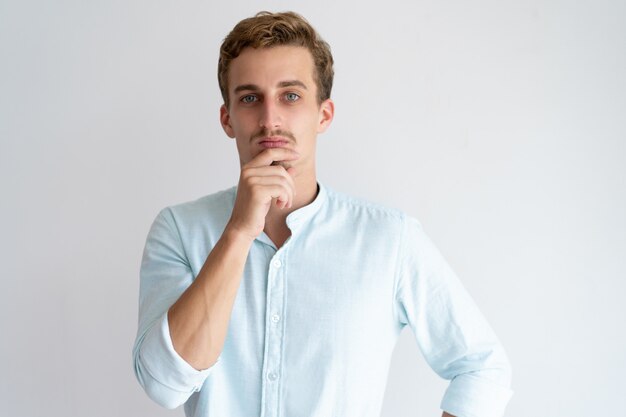 Pensive young man touching chin and looking at camera