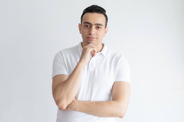 Pensive young man touching chin and looking at camera