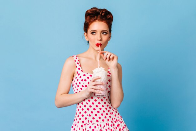 Задумчивая молодая женщина пьет напиток. Студия выстрел девушки кинозвезды имбиря, наслаждаясь молочным коктейлем.