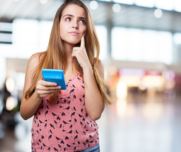 pensive young woman holding a calculator on white background