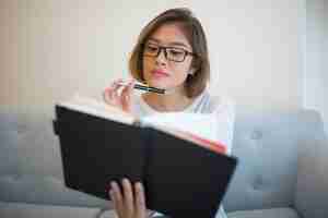 Free photo pensive young woman reading book on sofa at home