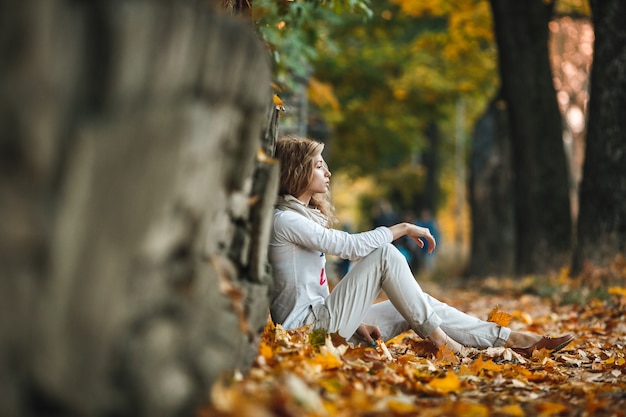 Pensive young woman sitting on dry leaves