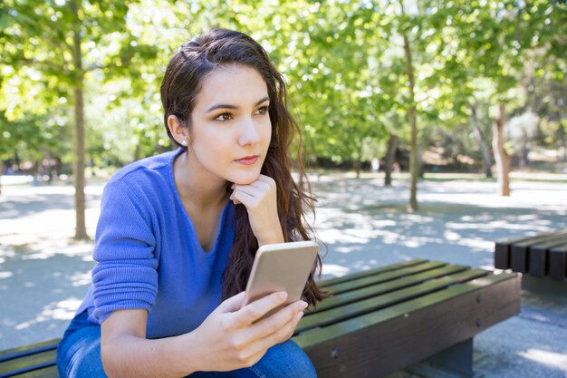 公園でスマートフォンを使用して物思いにふける若い女性