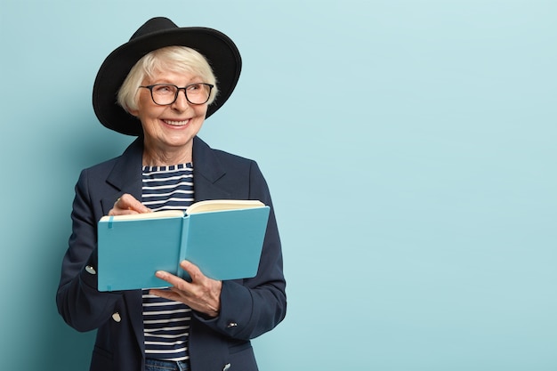 Foto gratuita persone, età, concetto di tempo libero. la femmina senior felice sulla pensione scrive la lista da fare nel suo blocco note blu