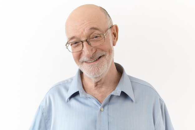 People, age, positiveness, joy and happiness concept. Handsome cute elderly man wearing blue shirt and rectangular eyeglasses smiling broadly, laughing at his own joke, expressing positive emotions