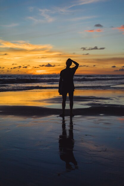 夕日のビーチにいる人たち。女の子は夕日を背景にして飛び降りています。