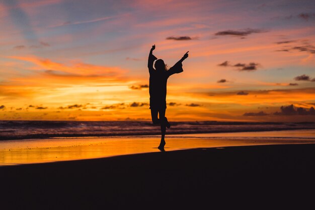 夕日のビーチにいる人たち。女の子は夕日を背景にして飛び降りています。