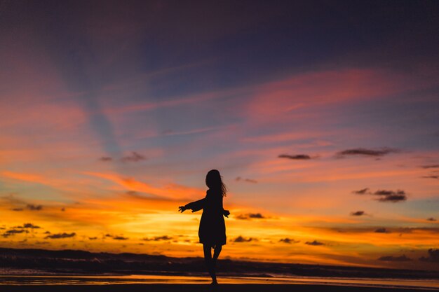夕日のビーチにいる人たち。女の子は夕日を背景にして飛び降りています。