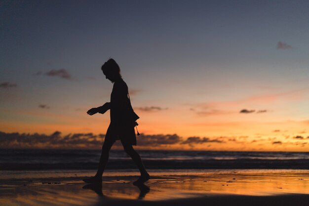 夕日のビーチにいる人たち。女の子は夕日を背景にして飛び降りています。