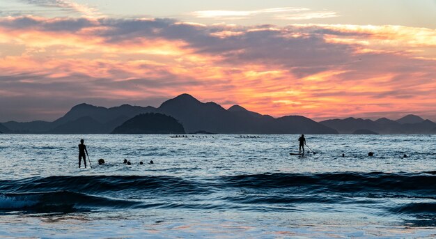 日没時に丘のシルエットで海のボートに乗っている人々