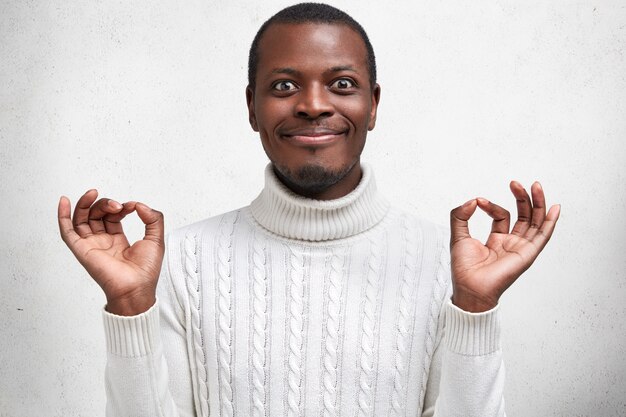 People, body language and positive emotions concept. Happy handsome African American male stands in mudra pose, has delighted look