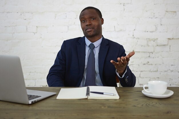 People, business, human facial expressions and reaction concept. Indoor shot of handsome dark skinned male entrepreneur wearing formal suit having frustrated puzzled look, gesturing indignantly