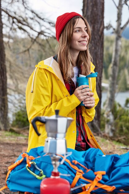 사람과 캠핑 개념. 만족 한 여성 여행자는 하이킹 후 보온병에서 뜨거운 음료를 마신다